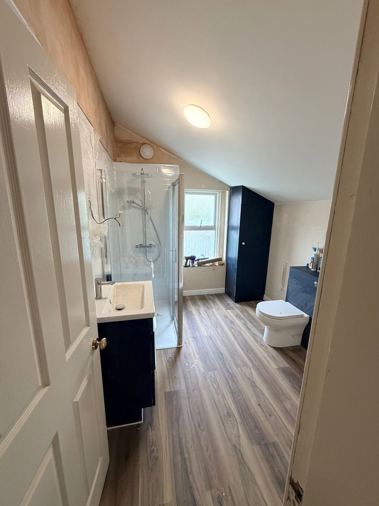 Loft bathroom conversion with fitted navy units and wood floor